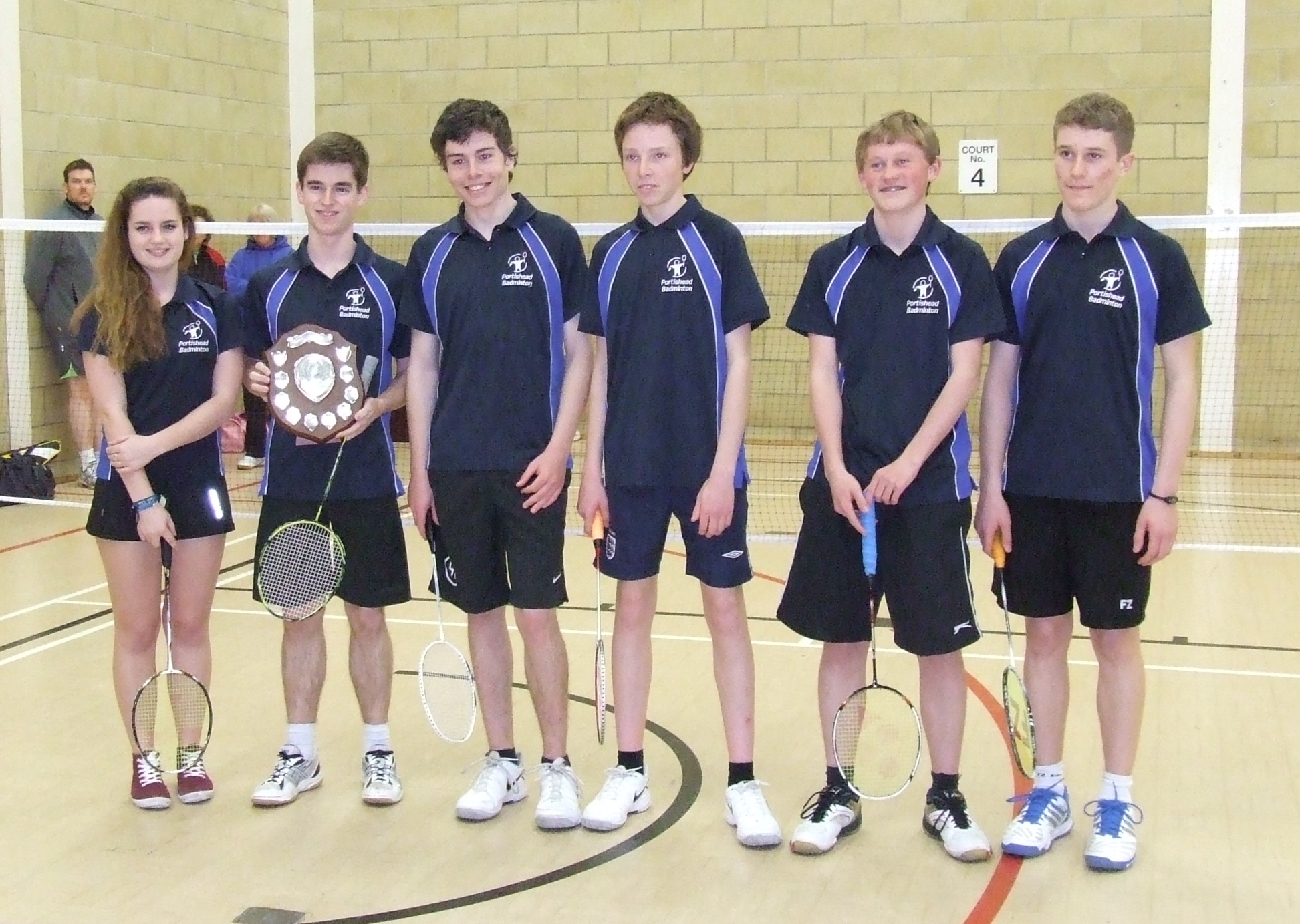 A neatly folded stack of deep blue jerseys with white accents, sitting on a wooden bench in a locker room. The jerseys are...