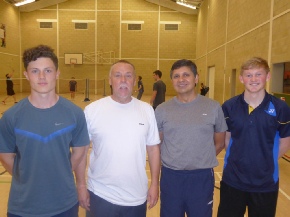A collection of silver and gold trophies displayed on glass shelves in a dark wooden case.
